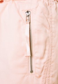 Tela rosa claro con textura de rayas verticales, que presenta un bolsillo con cremallera plateada y una lengüeta de tela en el lado derecho.