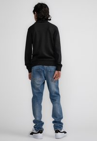 Maglione nero a maglia con colletto alto, abbinato a jeans in denim azzurro chiaro con vestibilità morbida e due tasche posteriori. Sneakers bianche e nere.