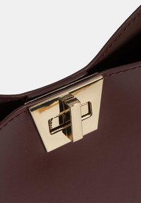 Kastanjebruine leren handtas met een goudkleurige rechthoekige sluiting en strakke lijnen, die de gladde textuur en minimalistische ontwerpdetails benadrukken.