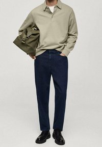 Jasnooliwkowa koszulka polo, ciemnoniebieskie dżinsy, czarne buty i oliwkowa torba na ramię. Prosty, codzienny strój o czystym designie.