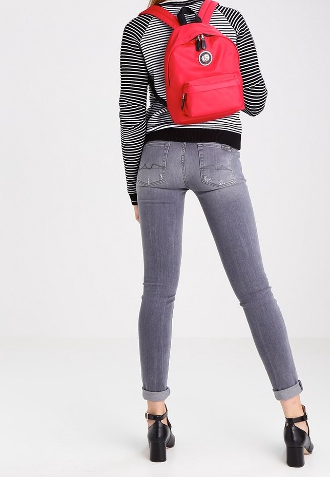 Rosa ryggsäck med rundad form, ficka med dragkedja fram och logopatch. Bärs över en svart och vit randig tröja med figurnära passform och grå jeans.