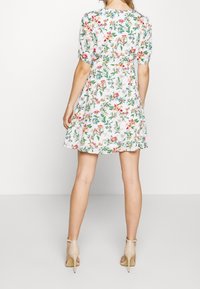Vestido blanco con estampado floral en varios colores, de mangas cortas y falda acampanada. Llevado con sandalias de tacón alto beige.