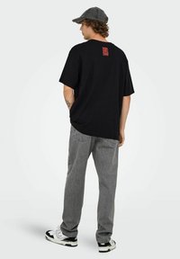 Camiseta negra de algodón con un gráfico rojo en la parte posterior, combinada con pantalones de mezclilla gris y zapatillas blancas con acentos negros.