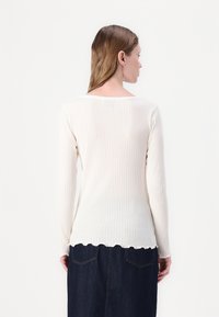 Maglia a maniche lunghe in crema a coste con scollatura ampia e orlo scallop, abbinata a una gonna in denim scuro. Texture liscia, senza motivi visibili.