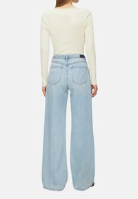 Hellblaue weit geschnittene Jeans aus Denim, mit einer hohen Taille, fünf Taschen und einem Rückeneinsatz, kombiniert mit einem eng anliegenden cremefarbenen Oberteil.