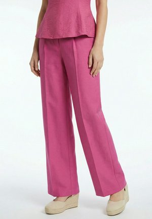 Frau trägt hoch taillierte, weit geschnittene rosa Hose mit passendem strukturiertem Oberteil und beigen Espadrilles mit Keilabsatz.