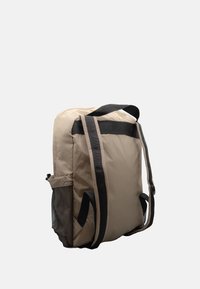 Zaino beige con una texture liscia, spalline nere regolabili e una tasca laterale in rete per ulteriore spazio di stivaggio. Design semplice e funzionale.