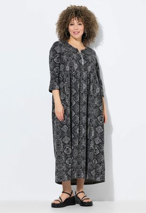 Zwart-wit slangenprint jurk met driekwart mouwen, een ronde halslijn en een knoopdetail op de borst. Model draagt zwarte sandalen.