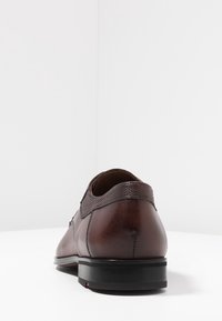 Chaussure en cuir marron avec une finition lisse, des accents texturés au talon et une semelle en caoutchouc noire. Vue de profil latéral mettant en valeur la forme.