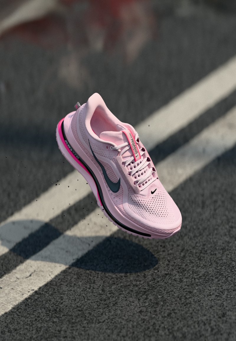 Chaussure de course Nike Pegasus rose en plein air au-dessus d'une route en asphalte avec une ligne blanche, projetant une ombre au sol.
