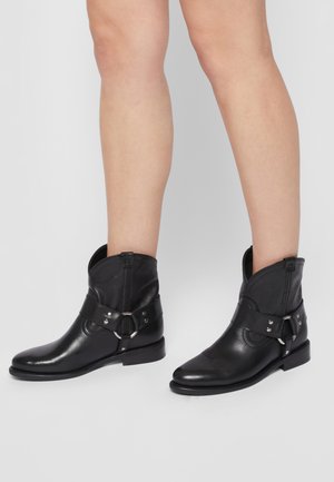 Botas de tobillo de cuero negro con punta redonda, cremallera lateral y detalle de correa con hebilla. Textura suave y tacón bajo apilado.