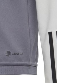 Grijze sportshirt van gladde stof, met contrasterend witte panel en zwart "AEROREADY" logo met een wereldbolontwerp. Gelaagde zoomdetails.