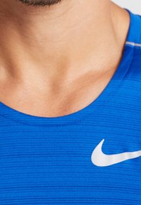 Nike Sportshirt in leuchtendem Blau, mit strukturiertem Stoff, rundem Ausschnitt und weißem Logo-Akzent auf der linken Brust.