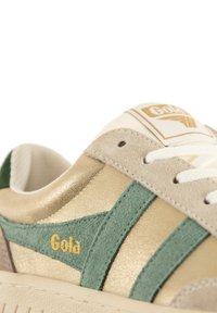 Sneakers Gola con un design in suede dorato metallico e verde, caratterizzati da un sistema di allacciatura bianco e una patch con logo sulla linguetta.