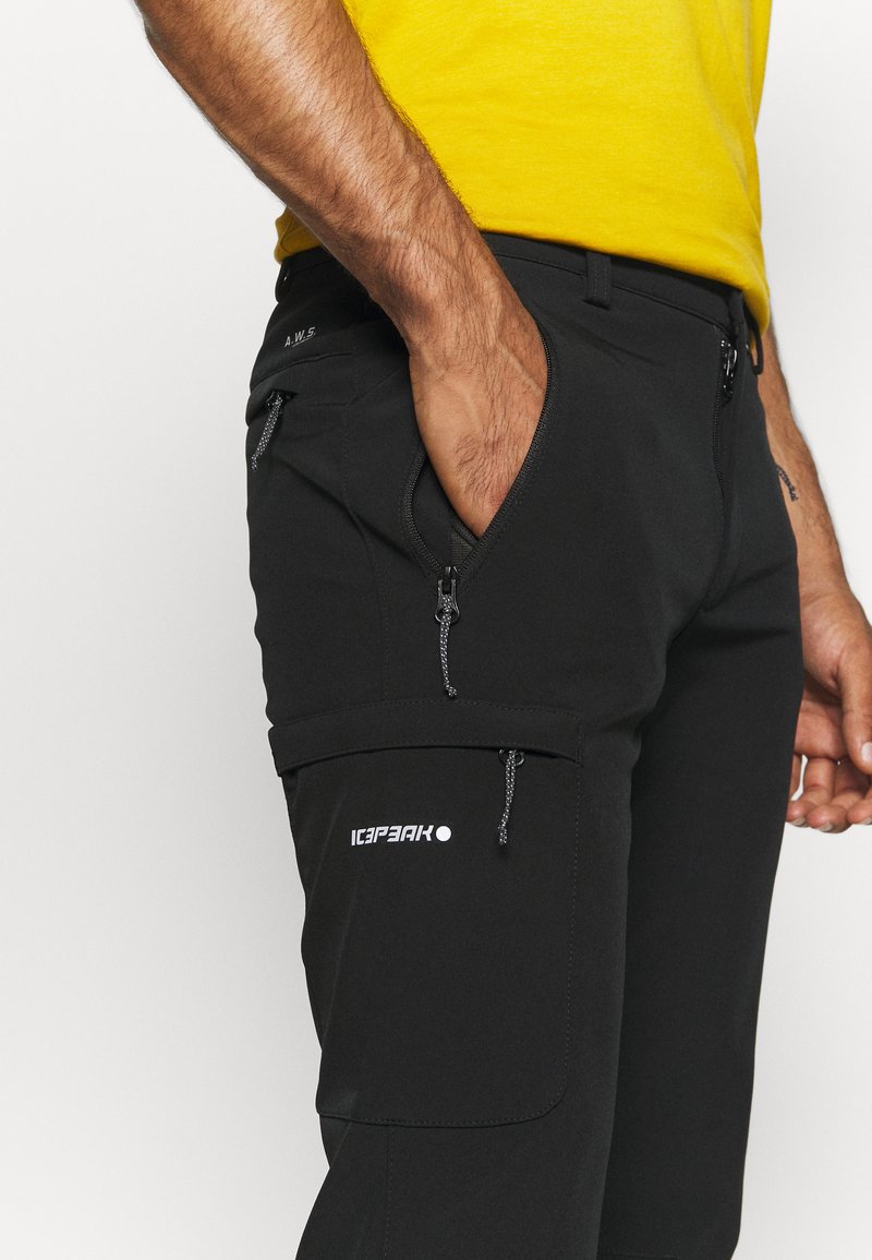 Zwarte outdoorbroeken hebben zijzakken met rits, verstelbare trekkoorden en een logo op de dij. Het materiaal is soepel en duurzaam.