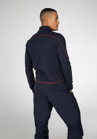 Maglione blu navy con collo alto, caratterizzato da dettagli in cucitura rossa, realizzato in tessuto testurizzato, abbinato a pantaloni scuri coordinati.