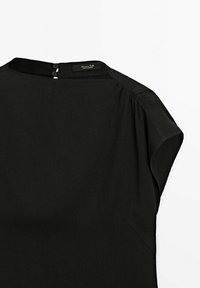 Schwarze Bluse mit hohem Hals, kurzen Ärmeln und subtilen Raffungen an den Schultern. Verfügt über einen zwei Knopfverschluss im Rücken.