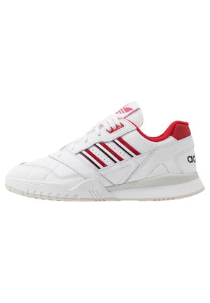 Chaussure de sport blanche avec des bandes rouges et noires, col rembourré rouge et semelle blanche, vue de côté extérieur.