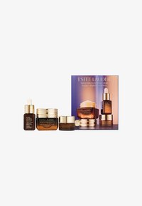 Estee Lauder hudvårdsset med en klar glasdropperflaska, burkar med guldaccent och en låda med en gradientdesign i lila och persika.
