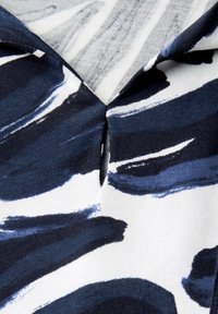 Top de manga corta con un patrón abstracto de pinceladas en azul marino y blanco, un cuello notch y una textura de tela suave y lisa.