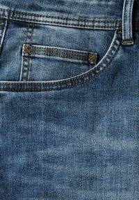 Denimtyg i en medelblå nyans med en blekt finish. Har synlig kontrastsömnad och en liten framficka.