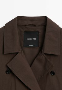 Brown trench coat featuring a notched collar, black buttons, and a fabric label with "Massimo Dutti." Material appears smooth with a matte finish.