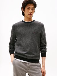 Maglione a motivi a coste neri con colletto rotondo e polsini a coste. Indossato sopra una camicia bianca, abbinato a pantaloni grigio chiaro.