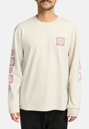 Mouwloze romige katoenen shirt met een voorzakafdruk van een zonontwerp. Heeft vergelijkbare zonafbeeldingen langs de mouwen.