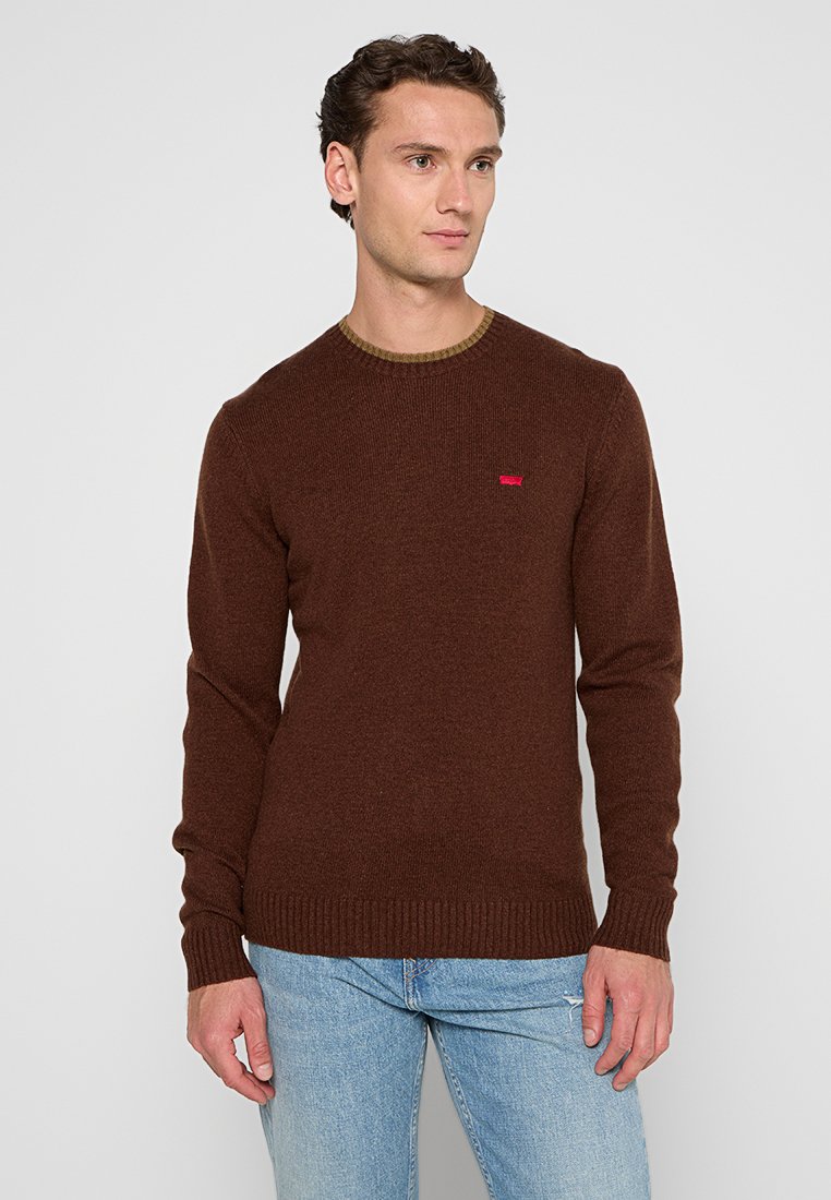 Brauner Pullover mit langen Ärmeln, geripptem Saum und rundem Ausschnitt. Besitzt ein kleines rotes Logo auf der Brust. Hergestellt aus strukturiertem Material.