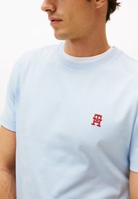 T-shirt in cotone azzurro chiaro con scollatura rotonda e maniche corte, che presenta un piccolo logo ricamato rosso sul petto.