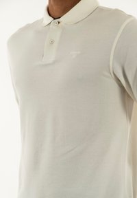 Witte polo-shirt van textuurstof, met een knoopsluiting van twee knopen en een klein logo op de linkerborst. Klassiek ontwerp van de kraag.