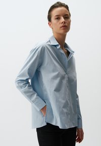 Camicia button-up azzurra chiara in cotone, con colletto classico, maniche lunghe e una vestibilità rilassata con fessure laterali.