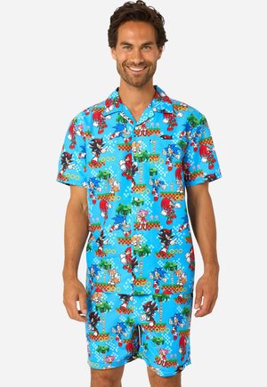Smiling man wearing bright blue Sonic the Hedgehog-themed short-sleeve shirt and matching shorts with multiple character prints.
