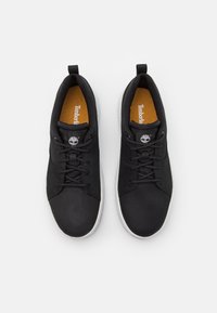 Une paire de sneakers Timberland noires avec des semelles blanches, des lacets noirs et des semelles intérieures orange, vues du dessus sur un fond blanc.