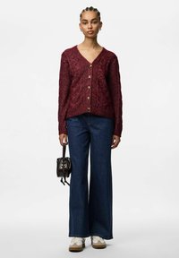 Burgundy kabelstickad cardigan med V-ringning, ribbade ärmslut och fem knappar i guldton. Kombinerad med vida blåjeans och vita sneakers.