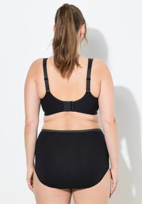 Zwarte bh met verstelbare bandjes en een haaksluiting, gecombineerd met hoge zwarte onderbroek met een stippenelastieken tailleband.