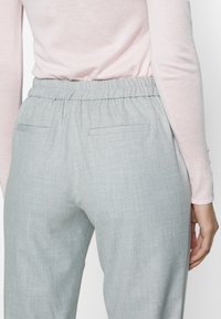 Grijze elastische broek met een textuurstof en twee achterzakken, gecombineerd met een lichtroze langmouwen top.