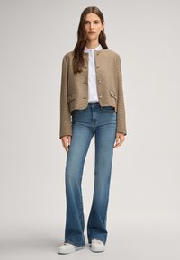 Beige geruite cropped jacket met ronde halslijn, knoopsluiting en voorzakken, gecombineerd met blauwe flared jeans en witte sneakers.