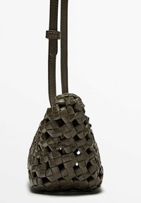 Vävd läderväska i mörkgrön, med triangelform, två justerbara remmar och en texturerad yta med ett öppet vävmönster.