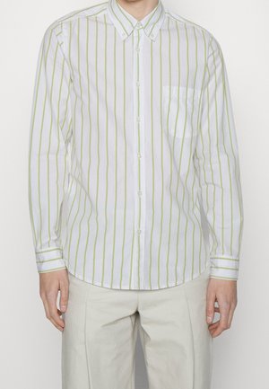 Mężczyzna w białej koszuli zapinanej na guziki z jasnobeżowymi pionowymi paskami i kieszenią na piersi, w połączeniu z jasnobeżowymi spodniami.