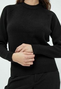 Črna pletena jopica z rebrastim okroglim izrezom, raglan rokavi ter rebrastimi manšetami in robom. Gladka tekstura, prilegajoča oblika in minimalističen dizajn.