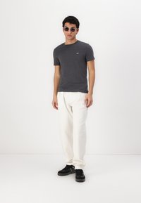 Tricou gri cu guler rotund, asortat cu pantaloni albi, lejeri, și adidași negri. Accesoriile includ ochelari de soare întunecați.