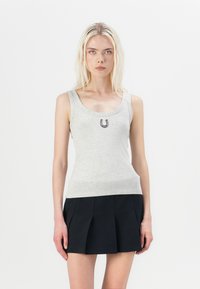 Top sin mangas de color gris claro con escote redondeado y un diseño en forma de herradura en el centro, combinado con una falda plisada negra.