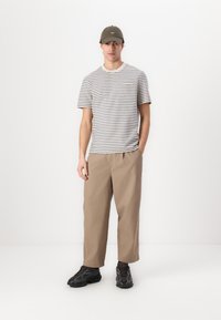 Tricou cu dungi în bej deschis și bleumarin, pantaloni lejeri bej, și adidași negri. Căciula este de culoare verde măslin. Design simplu cu o croială confortabilă.