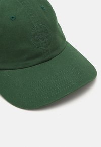 Zöld baseball sapka hímezett logóval, texturált anyaggal és ívelt vízlepergetővé. A dizájn a korona szellőzőlyukait is tartalmazza.