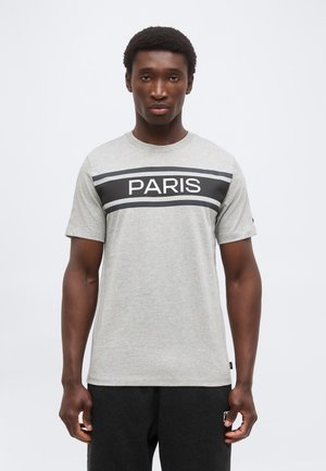 Homme debout face à l'avant portant un t-shirt gris clair avec « PARIS » en blanc sur une bande horizontale noire au niveau de la poitrine.