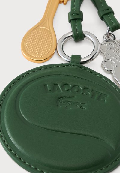 Porte-clés Lacoste en cuir vert en forme de balle de tennis avec une raquette de tennis dorée et un charm crocodile argenté attachés.