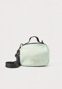 Mēnesta zaļas krāsas kompakta somiņa ar mīkstu tekstūru, melnu siksnu, augšējo rokturi un reljefu logotipu priekšpusē. Aizdare ar rāvējslēdzēju.