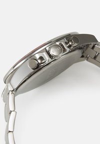 Montre en acier inoxydable argenté avec un boîtier rond, trois boutons-poussoirs et un bracelet en maillons polis. Marque 'BOSS' notable sur la couronne.