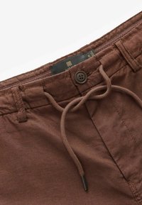 Braune Leinenmischungshose mit einem Kordelzugbund, Knopfverschluss und sichtbarem Innenetikett; strukturierter Stoff mit glatter Oberfläche.